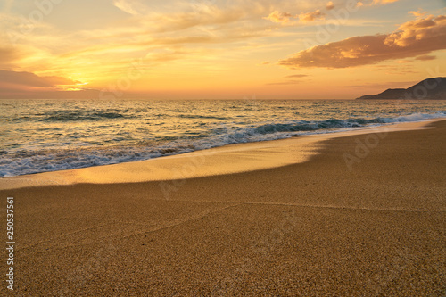 Colorful sunset at the tropical sandy beach, waves with foam hitting sand. Copy space.