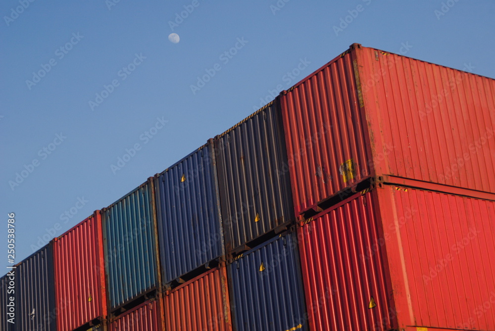 Linha de contentores no céu, contentores empilhados, azuis e vermelhos com céu de fundo e lua á luz do dia, exportações, importações Linha de contentores no céu, contentores empilhados, azuis e vermelhos com céu de fundo e lua á luz do dia, exportações, importações
