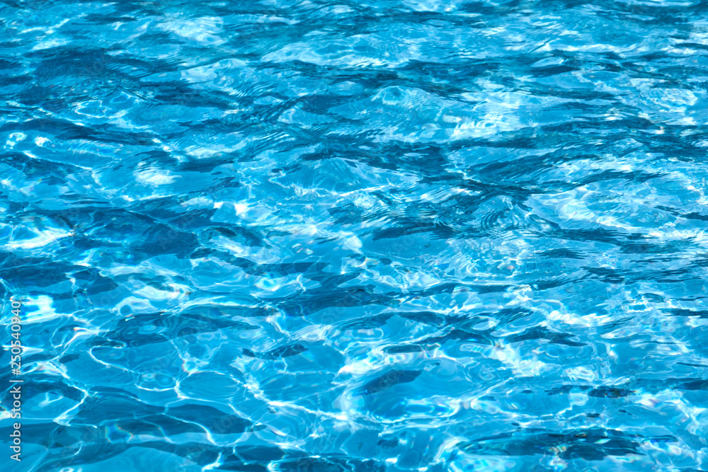 Blue and bright ripple water surface in swimming pool with sun reflection.