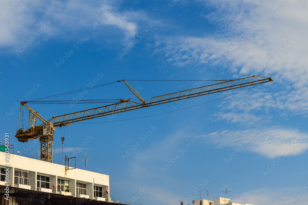 Luffing jib tower crane at large scale construction site over steel framework among high rise building. Skyscraper building construction with the tower cranes on top under the dramatic sky background.