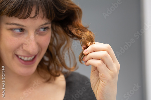 Girl's face with a lock of hair in her hands looking at split ends