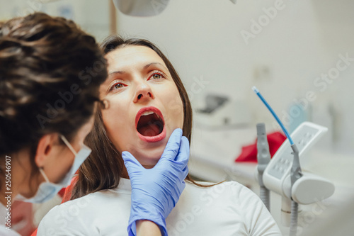 Fototapeta Naklejka Na Ścianę i Meble -  Young woman sitting in a dental chair for appointment of a doctor. During this time, she was very worried about fear, opened her big eyes. A doctor is a good woman in medical clothes, which makes a