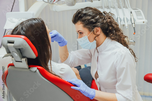 Young woman sitting in a dental chair for appointment of a doctor. During this time, she was very worried about fear, opened her big eyes. A doctor is a good woman in medical clothes, which makes a