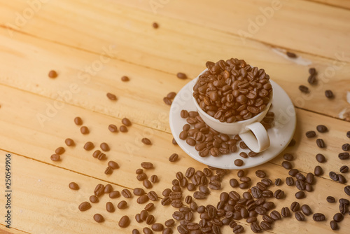 White cup full of coffee beans on Roasted Coffee Beans and wood background  top view