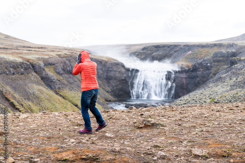 Thorufoss waterfall windy landscape on Golden Circle in Iceland with water flowing on rocks river from cliff and woman tourist in jacket and jeans holding head