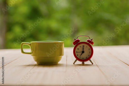 green coffee cup with red alarm clock with nature background