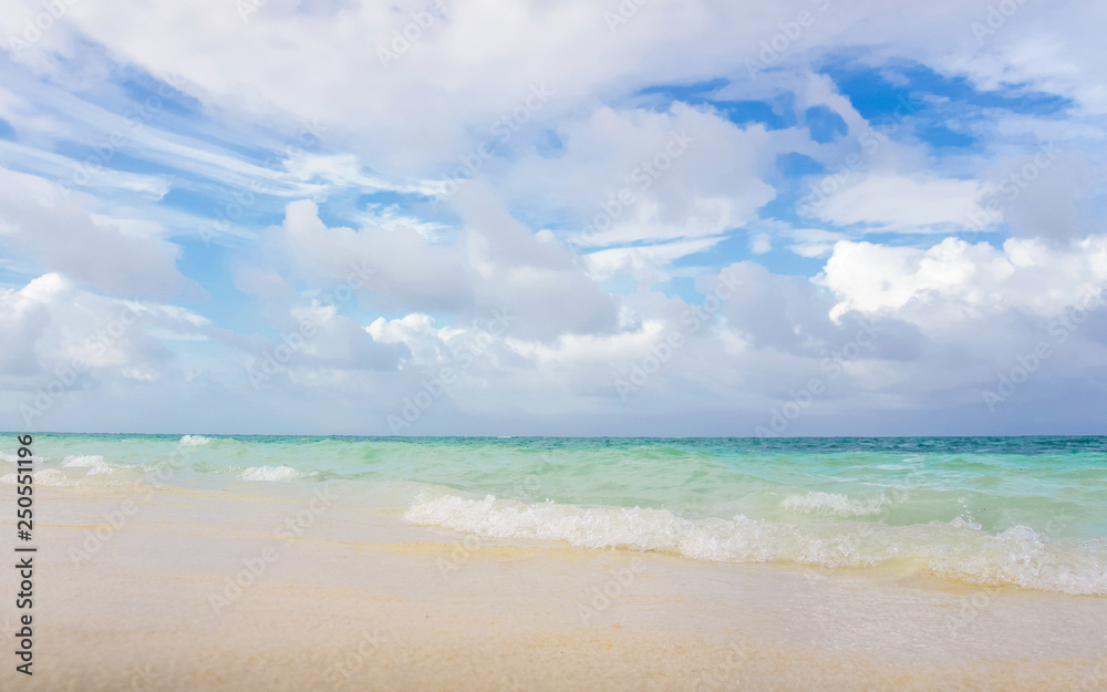 Sunny tropical beach with blue sky and scattered white clouds and clear water