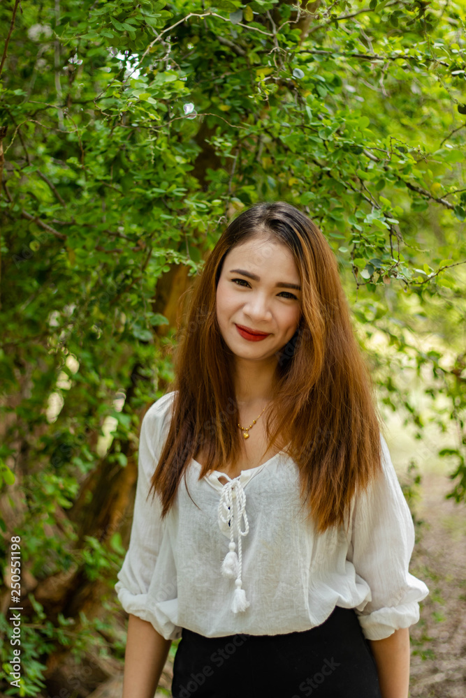 Women white skin lovely brown hair red lip wear white shirt women standing poses photography portrait In the garden has a tree as a background. Women white skin lovely brown hair red lip wear white shirt women standing poses photography portrait In the garden has a tree as a background.
