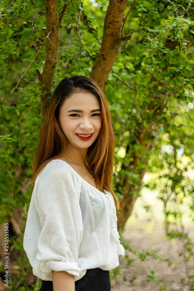 Women white skin lovely brown hair red lip wear white shirt women standing poses photography portrait In the garden has a tree as a background. Women white skin lovely brown hair red lip wear white shirt women standing poses photography portrait In the garden has a tree as a background.