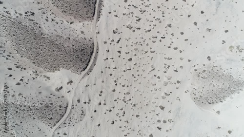 Aerial drone scene top view, senital, of desert with bright clear beige sand and few green plants. gravel road covered by sand. Camera moving forward. Taton, Catamarca Province, Argentina. photo