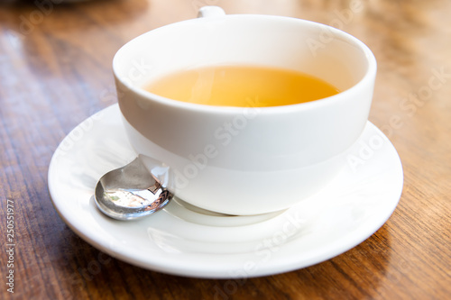 Closeup of one white cup on plate and green black or oolong tea in breakfast brunch cafe restaurant wooden table with spoon