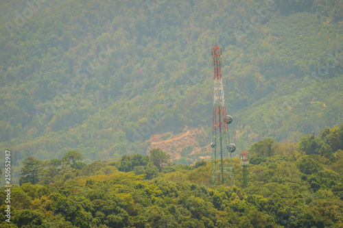 A tall telecommunication tower is standing in amid the green valley background. A telecom tower in a rural area needs off-grid power to transmit cell signals.