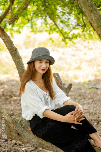 Women white skin lovely brown hair wearing a gray hat red lip wear white shirt wearing black pants women sit poses photography portrait under the tree In the garden.