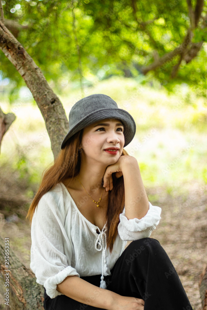 Women white skin lovely brown hair wearing a gray hat red lip wear white shirt wearing black pants women sit poses photography portrait under the tree In the garden.