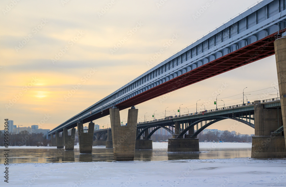 View of the Metro Bridge and the October Bridge over the Ob River. Novosibirsk, Siberia, Russia. Cold weather. The water is partially covered with ice. In the distance buildings. Place for text.