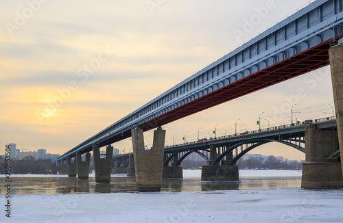 View of the Metro Bridge and the October Bridge over the Ob River. Novosibirsk, Siberia, Russia. Cold weather. The water is partially covered with ice. In the distance buildings. Place for text. © Andrei Stepanov