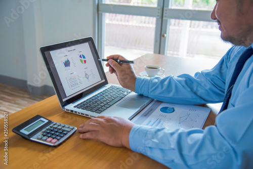 Business man working at office with laptop, tablet and graph data documents on his desk.