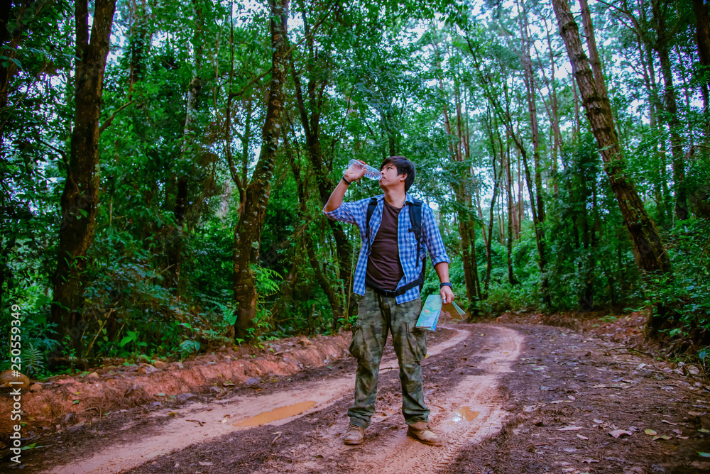 Happy hipster man tourist with backpack drinking water while hiking in nature forest.