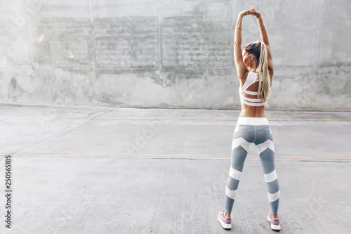 Obraz Sprawności fizycznej sporta kobieta w mody sportswear robi rozciągania ćwiczeniu nad szarości ścianą