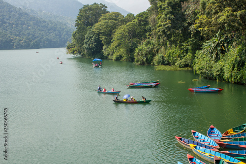 Fototapeta Naklejka Na Ścianę i Meble -  Pokhara/Nepal - 18.10.2018: People in multicolored wooden boats on the lake against the backdrop of the green jungle
