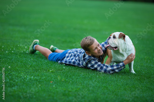 Little boy teenager with his dog bulldog in park on a sunny day on green grass park land enjoy life together with his friend