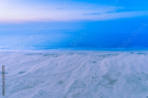 Aerial view of ocean coastline at dawn. Nothing but White sand, blue water and sky.