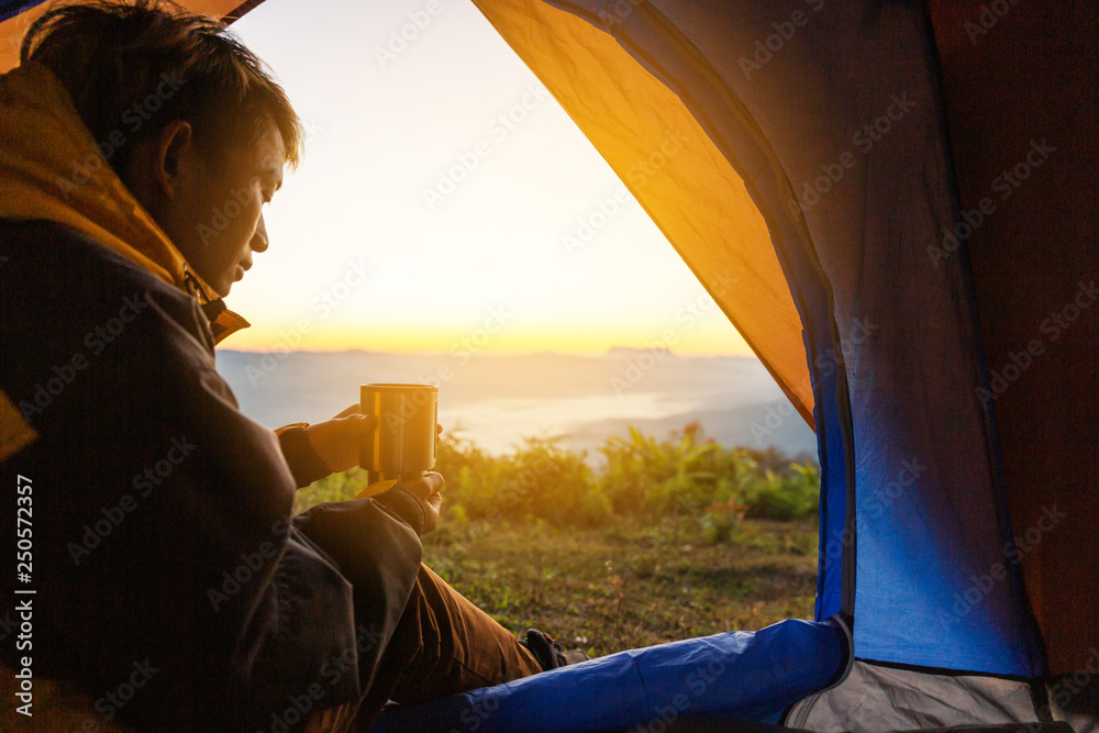 A young man sitting in the tent with holding coffee cup, looking at the mountain landscape in winter.Light effects