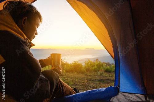 A young man sitting in the tent with holding coffee cup, looking at the mountain landscape in winter.Light effects