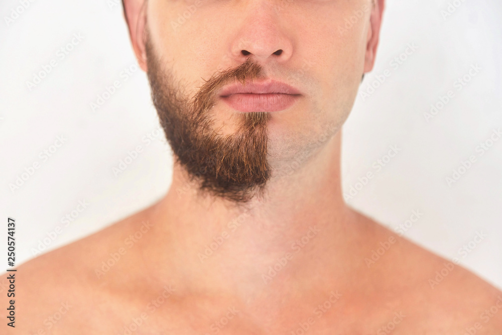Half shaved. A young man with beard on half of the face on light grey background. 