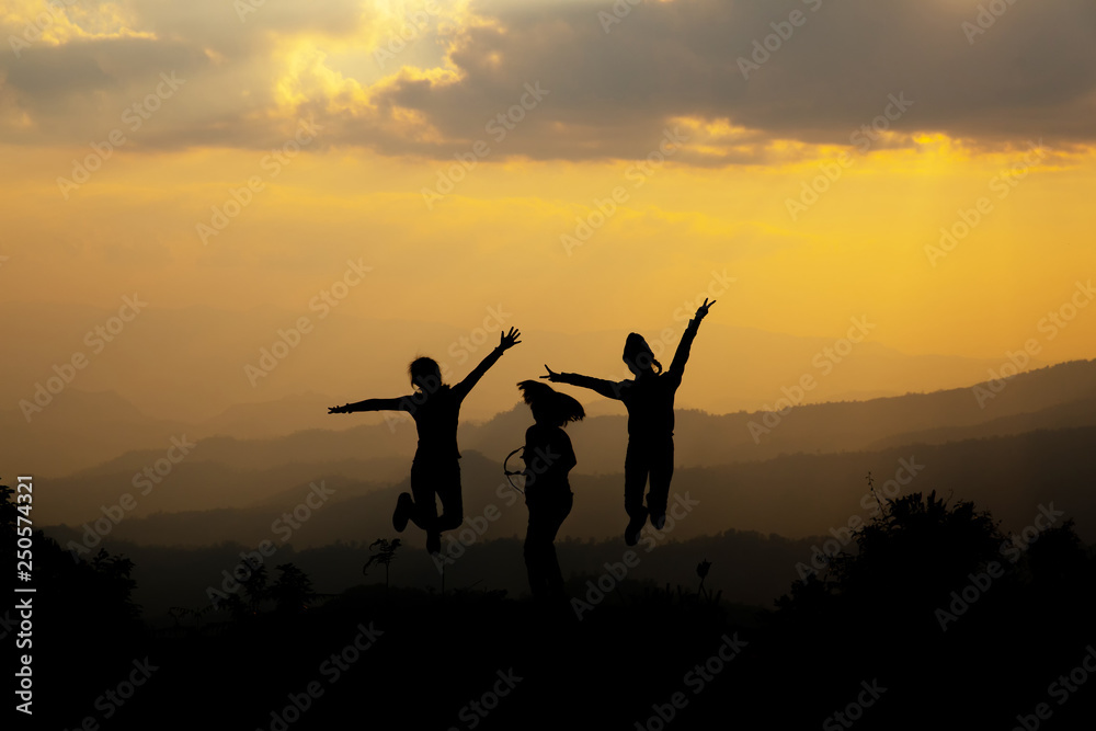 Group of happy people jumping in the mountain at sunset, concept about having fun on the hill, silhouette