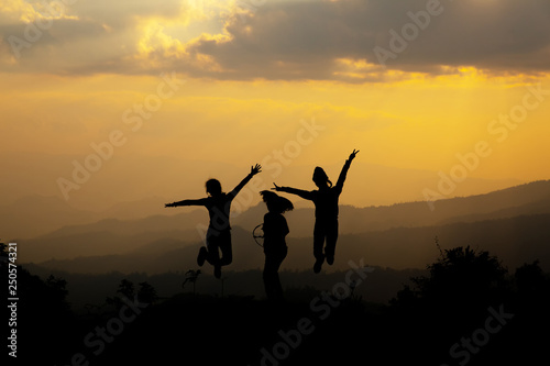 Group of happy people jumping in the mountain at sunset, concept about having fun on the hill, silhouette