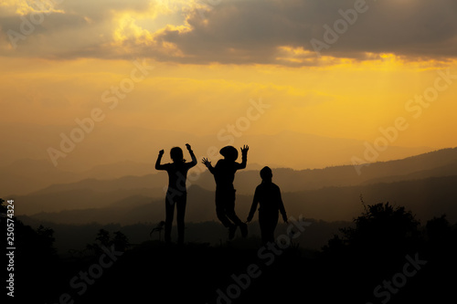 Group of happy people jumping in the mountain at sunset, concept about having fun on the hill, silhouette
