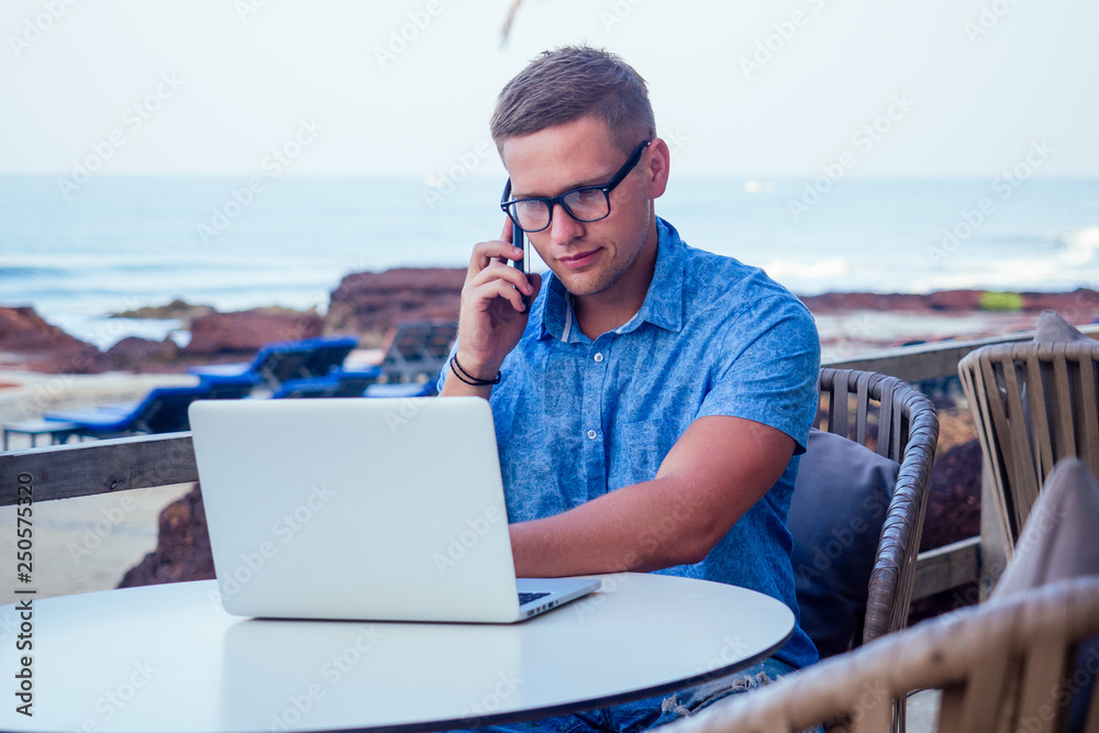 business man using laptop or netbook computer while seated at a cafe table outdoors talking on the phone.remote work