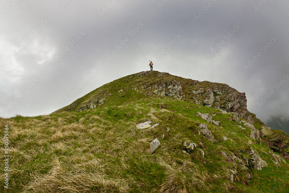 Man hiker stands on the top of mountain celebrating achievement of reaching the highest peak on Stara Planina mountain in Serbia.