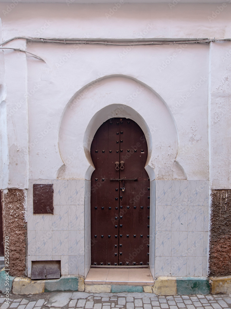Naklejka premium Traditional Moroccan style design of an ancient wooden entry door. In the old Medina of Marrakech, Morocco. Typical, old, brown intricately carved, studded, Moroccan riad door