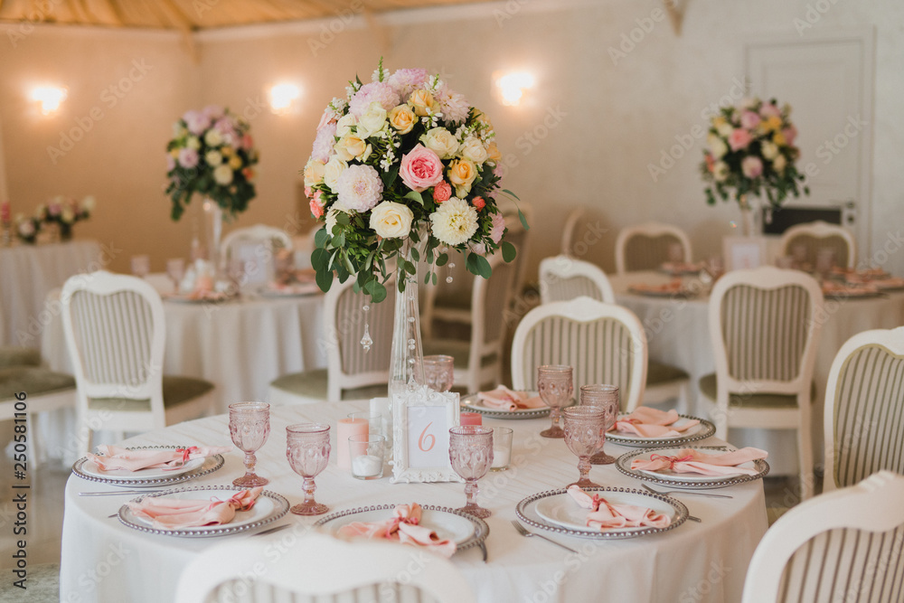 Coziness and style. Modern event design. Table setting at wedding reception. Floral compositions with beautiful flowers and greenery, candles, laying and plates on decorated table.