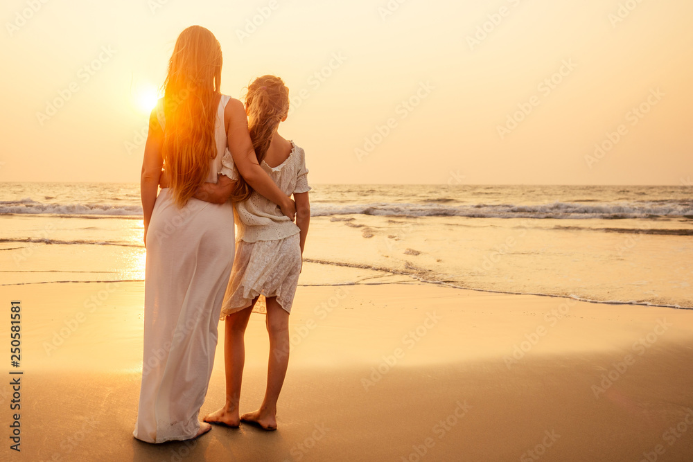 Little teenager cute girl and young mother long blonde hair at tropical beach enjoying the sunset on the sea tenderness and intimacy care