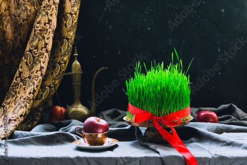 Novruz setting in Azerbaijan with black tea in armudu pear shape drinking glass with green wheat grass semeni with red ribbon for celebration. Spring equinox, Persian Nowruz greeting card copy space 