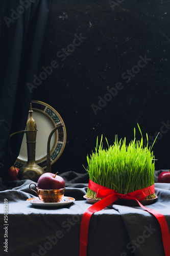 Novruz setting in Azerbaijan with black tea in armudu pear shape drinking glass with green wheat grass semeni with red ribbon for celebration. Spring equinox, Persian Nowruz greeting card copy space 