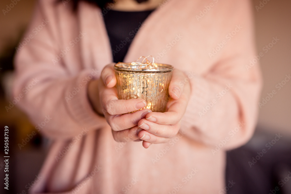 Fototapeta premium Junge Frau hält goldenes Glas mit Lichterkette