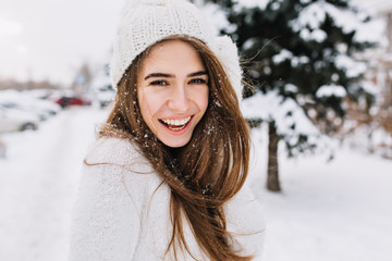 Spectacular long-haired woman laughing while posing on snow background. Outdoor close-up photo of caucasian female model with romantic smile chilling in park in winter day.