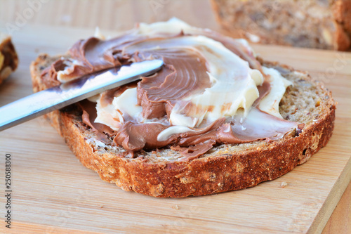 Chocolate and vanilla peanut butter creamy spread with hazelnuts on brown whole wheat bread slice