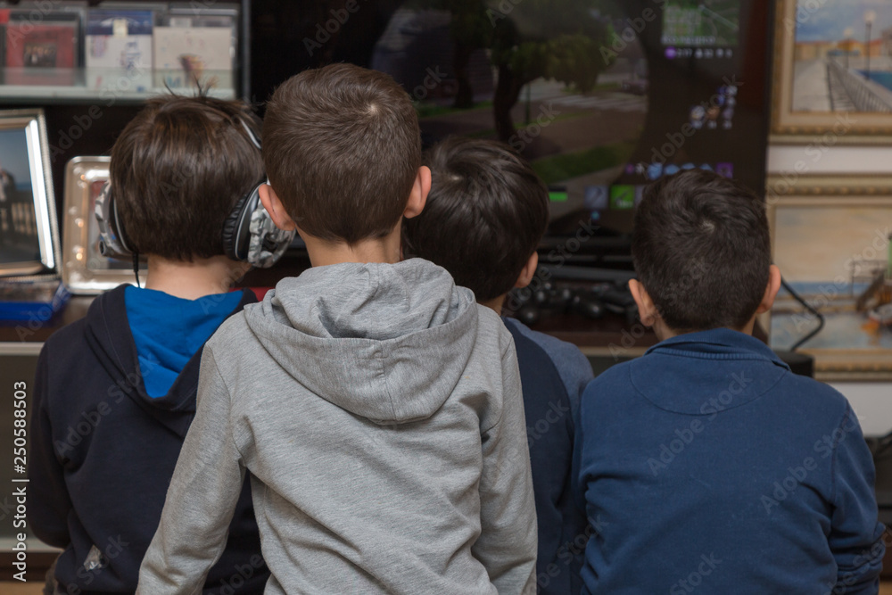 Ten year old Children Seen from behind Playing Video games while sitting in front of the Television