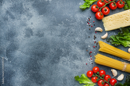 Raw Italian pasta spaghetti and cooking ingredients cherry tomatoes Cheese greens. Italian food dark stone background. Top view with copy space