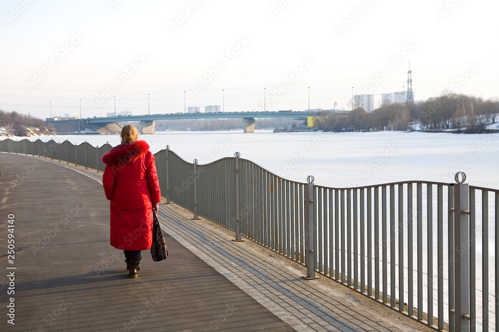 A lonely woman in a red coat walks along the promenade.