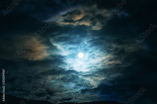 Full moon or supermoon in night blue sky with clouds, dramatic mysterious atmosphere