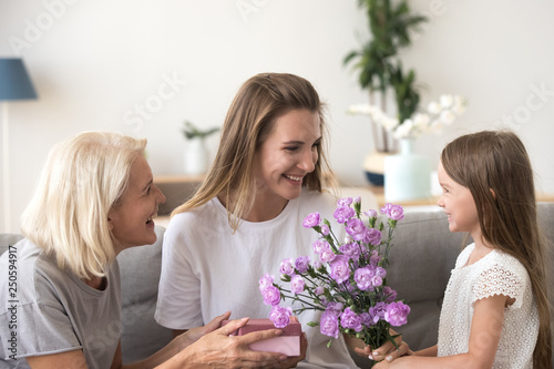 Happy mother receiving gift and bouquet from daughter and grandmother