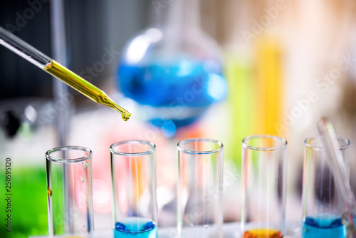 Using dropper sampling oil or chemical liquid drop to test tube with lab glassware in laboratory background, science or medical research and development concept
