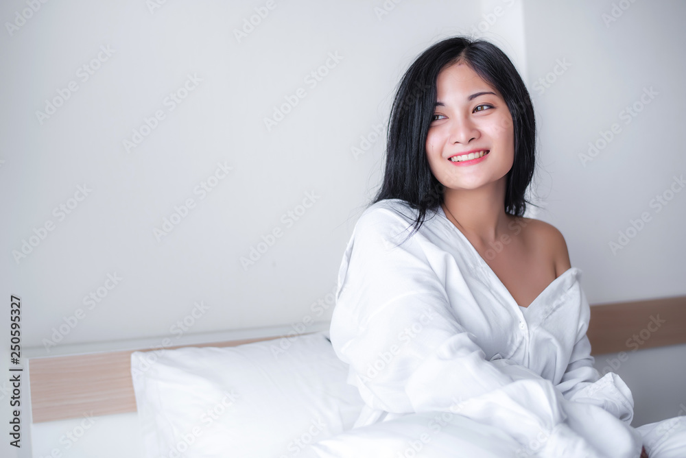 Beautiful young pretty Asian woman wake up and make happy smile with white shirt at the white bed in the morning. Beautiful young pretty Asian woman wake up and make happy smile with white shirt at the white bed in the morning.