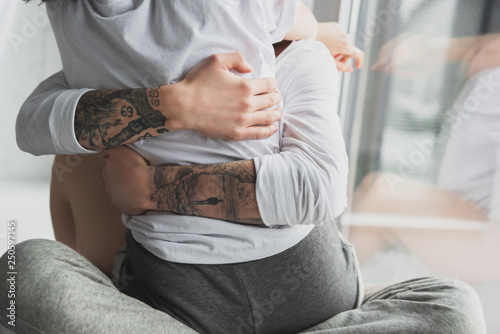cropped view of tattooed man passionately hugging woman at home